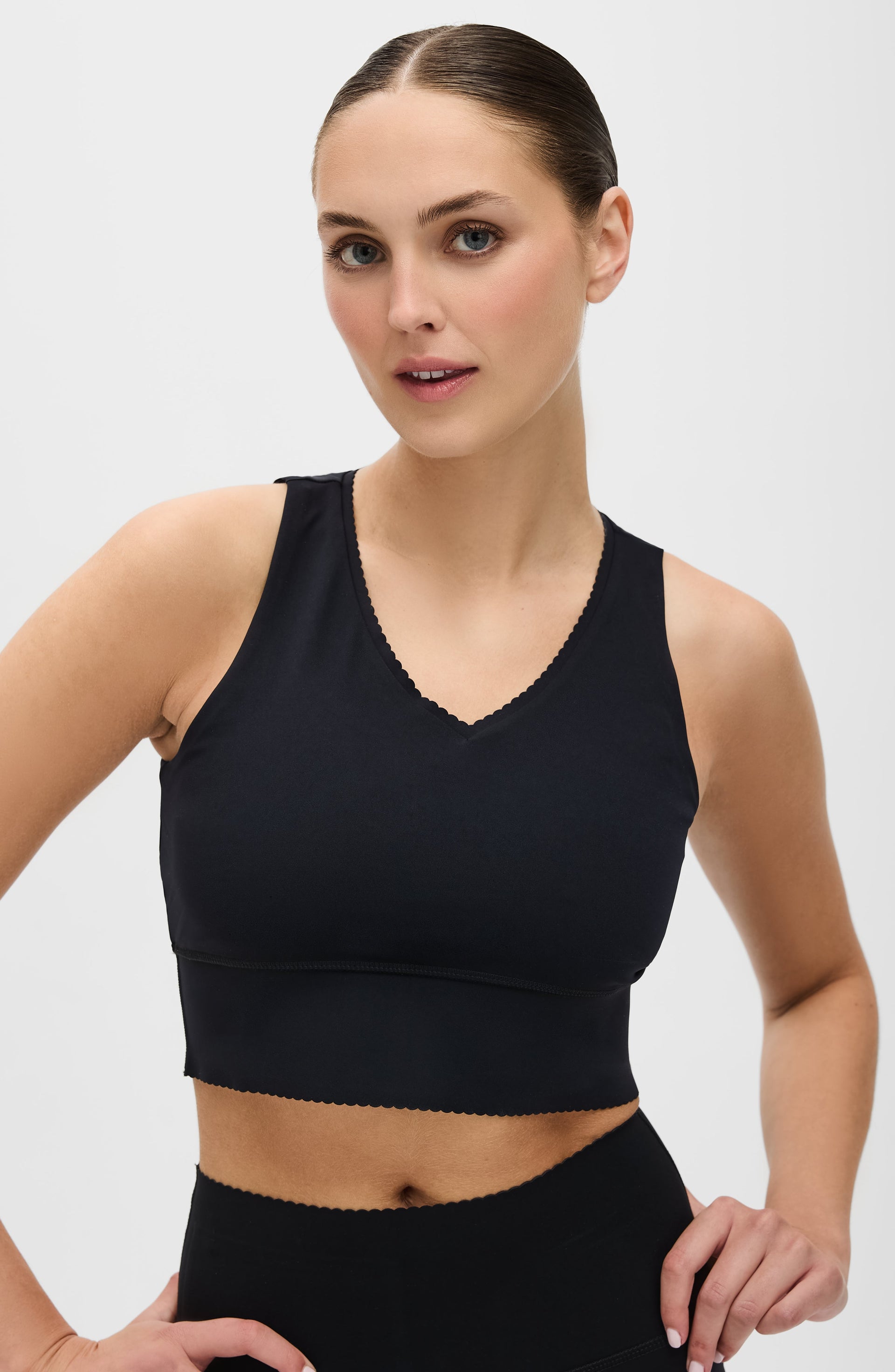 Woman wearing an Elastique Athletics black sports bra and leggings on a light gray background