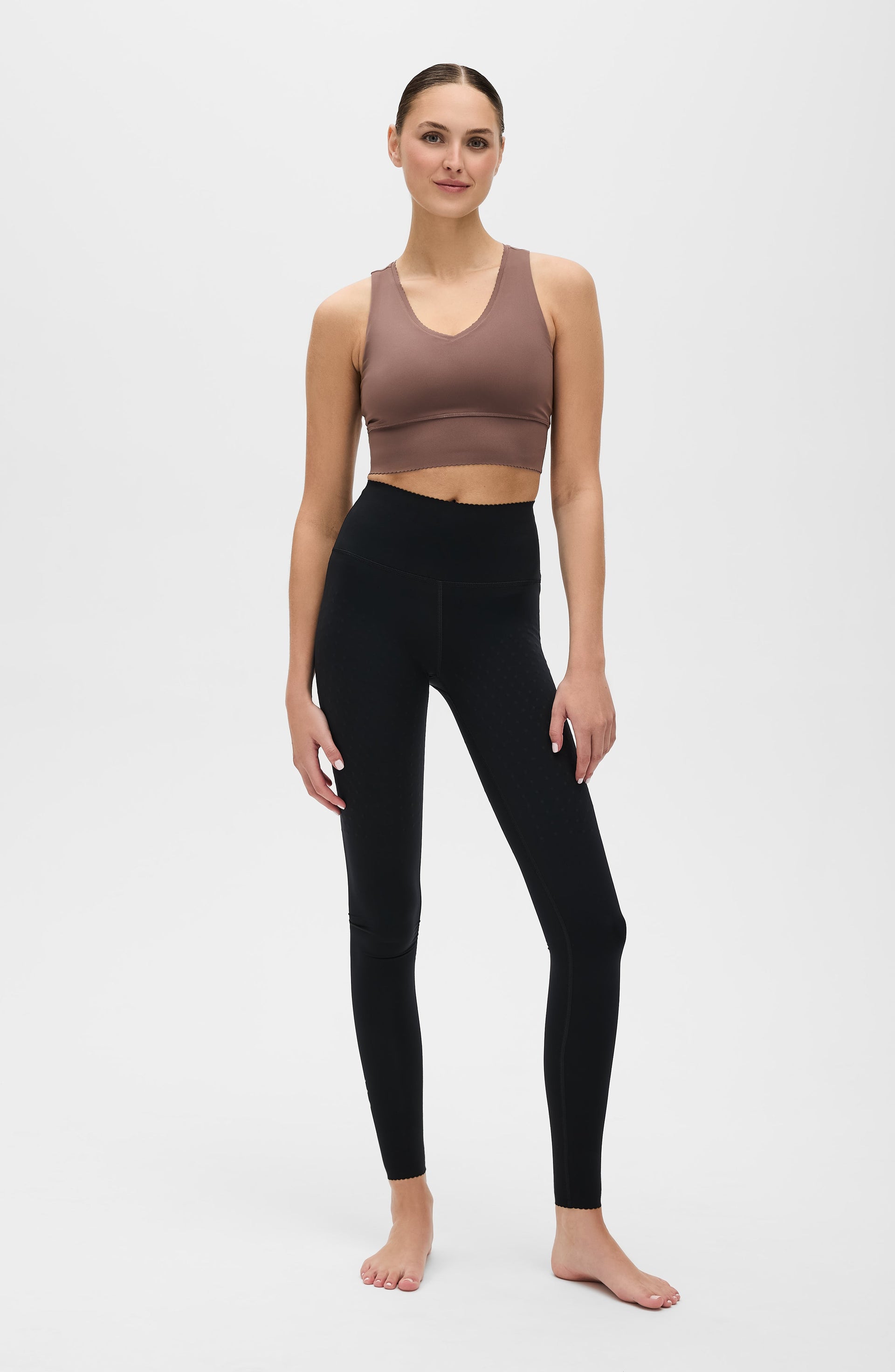 Full body studio portrait of a woman wearing the Elastique Athletics Adorn Leggings in black with a taupe sports bra.