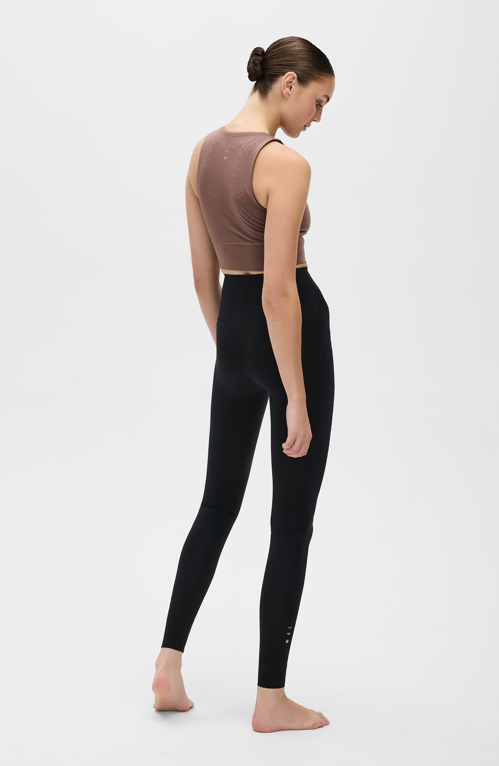 Woman wearing black an Elastique Athletics Adorn leggings and brown crop top on a white background