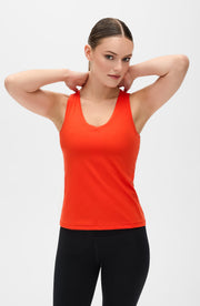 Woman posing with both hands behind her head while wearing the Elastique Athletics Adorn Tank in bright orange with black leggings.