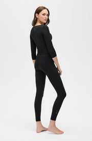 Full body side profile of a woman wearing the Elastique Athletics Iconic Sleeve MicroPerle Top in black with fitted leggings.