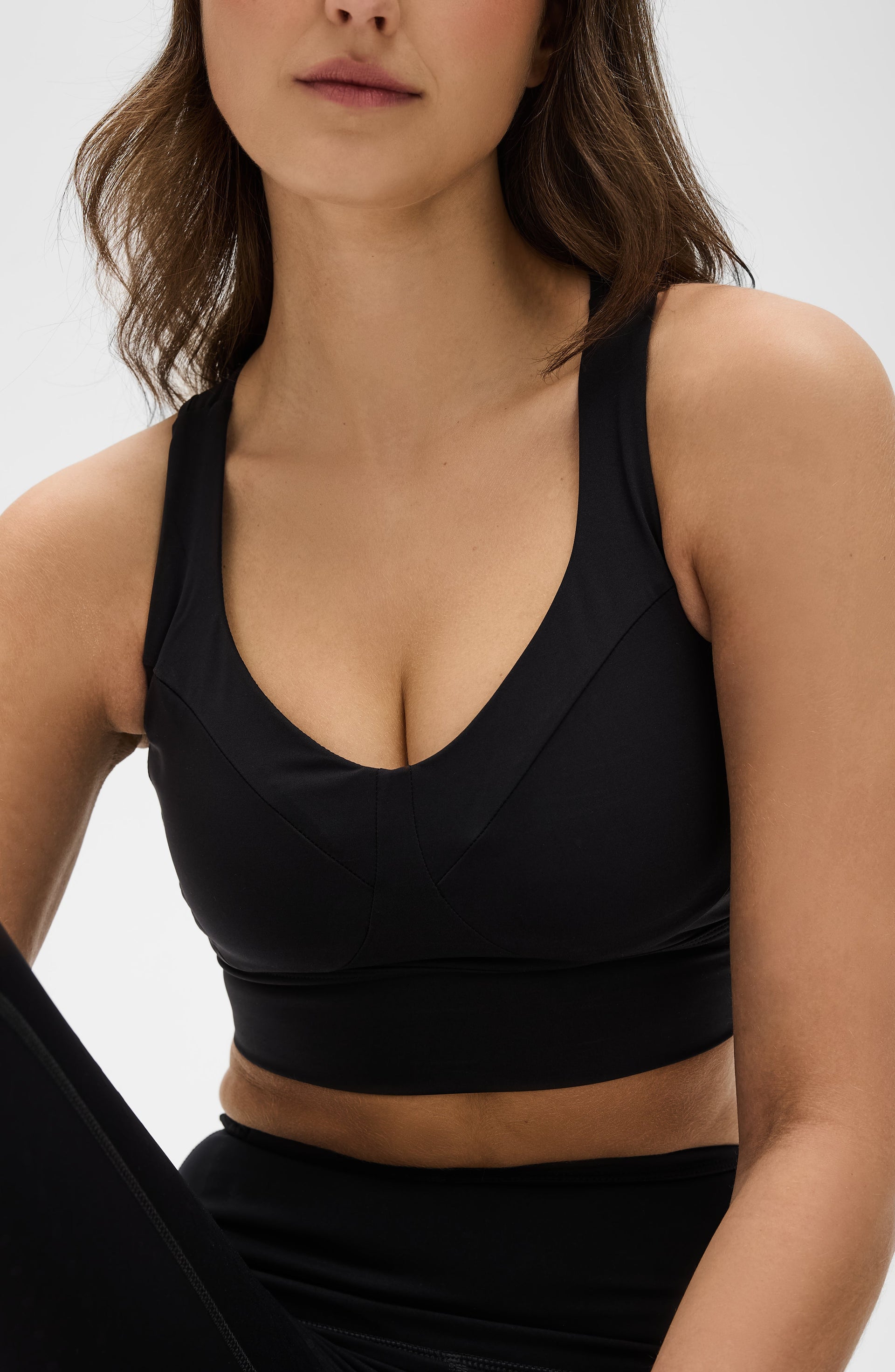 Close up portrait of a woman wearing the Elastique Athletics Le Divine Lymphatic Bra in black with a deep scoop neckline and matching leggings.