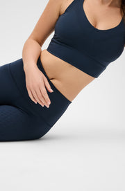 Woman seated on the floor wearing the Elastique Athletics Le Divine Lymphatic Bra in navy blue with matching leggings.