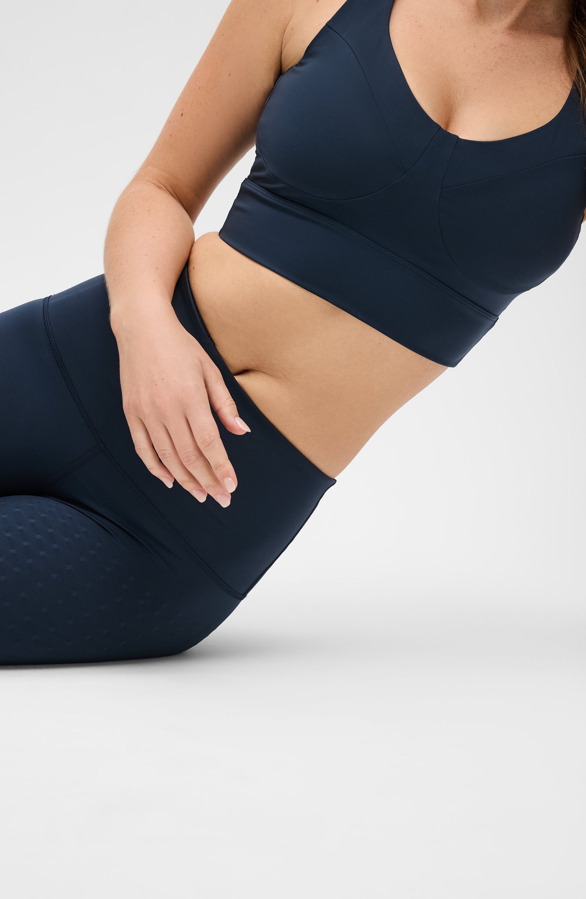 Woman seated on the floor wearing the Elastique Athletics Le Divine Lymphatic Bra in navy blue with matching leggings.
