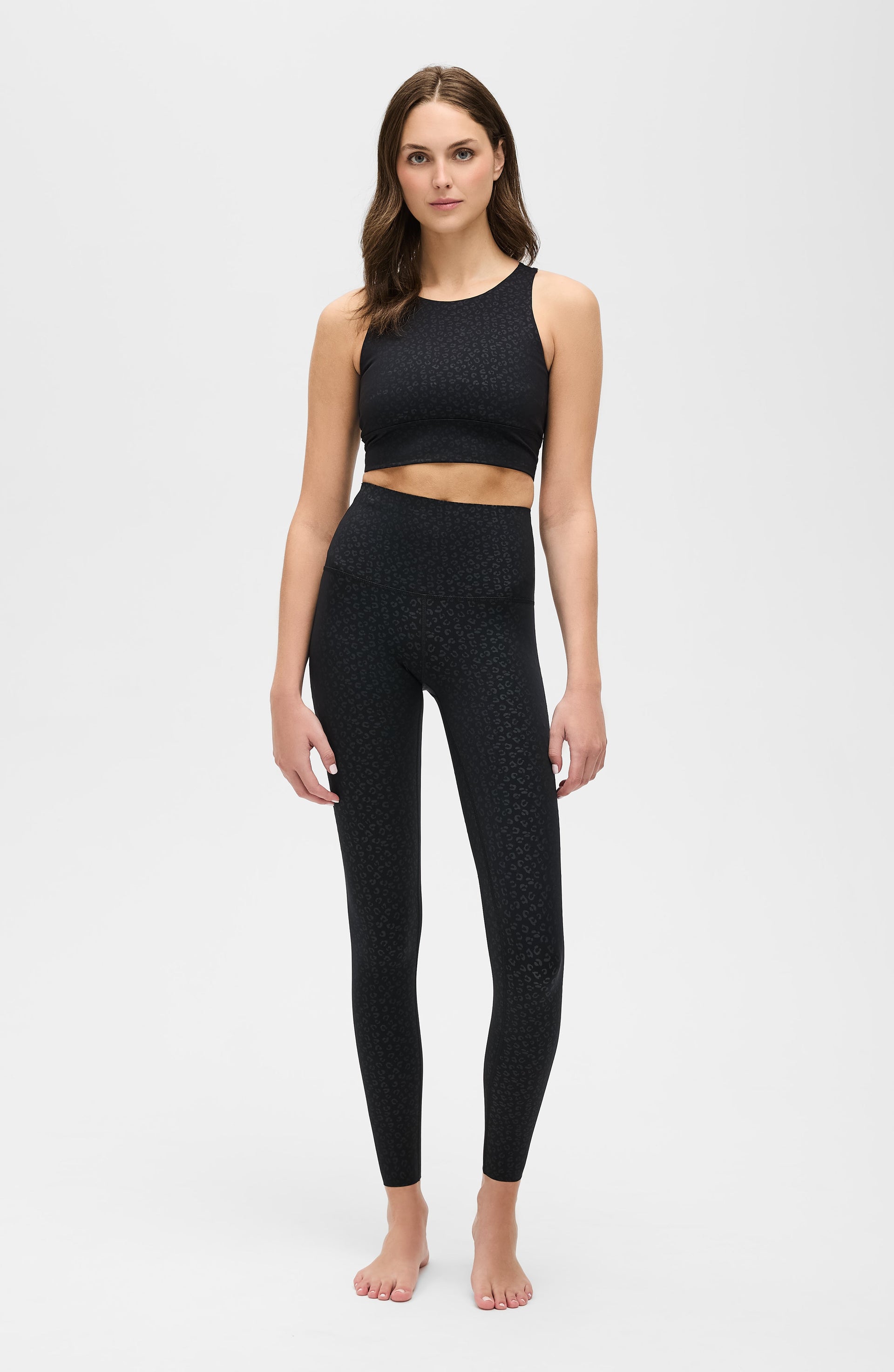 Full body studio portrait of a woman wearing the Elastique Athletics The Fierce Leggings in black with a matching sleeveless crop top.