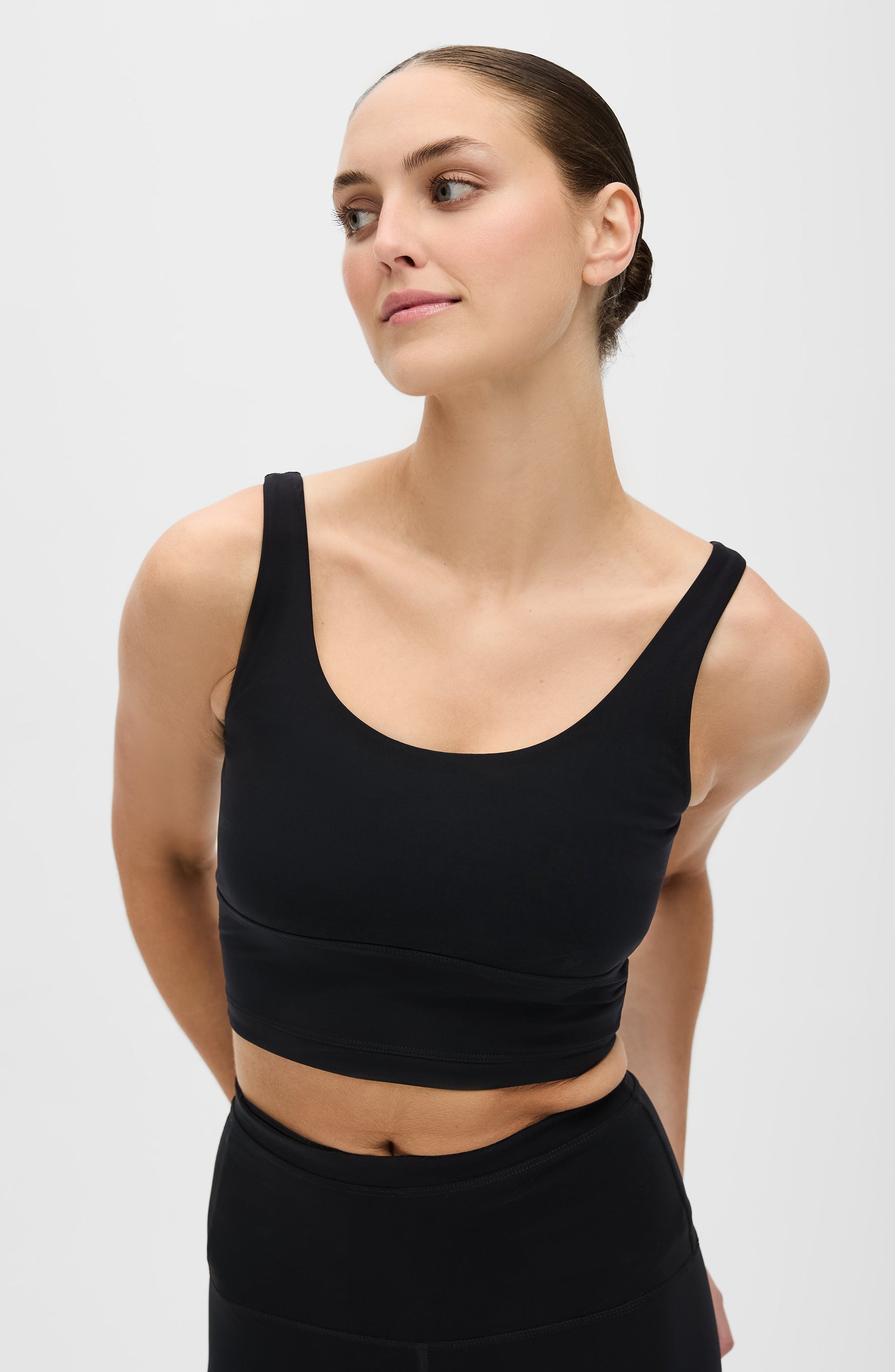 Woman posing with her hands behind her back while wearing the Elastique Athletics Lisse Compression Bra in black with matching leggings.