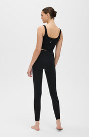 Back view of a woman standing barefoot while wearing the Elastique Athletics Lisse Compression Bra in black with matching leggings.