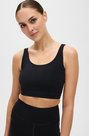 Close up portrait of a woman wearing the Elastique Athletics Lisse Compression Bra in black with a scoop neckline and matching leggings.