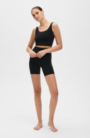 Full body studio portrait of a woman wearing the Elastique Athletics Lisse Compression Bra in black with matching biker shorts.