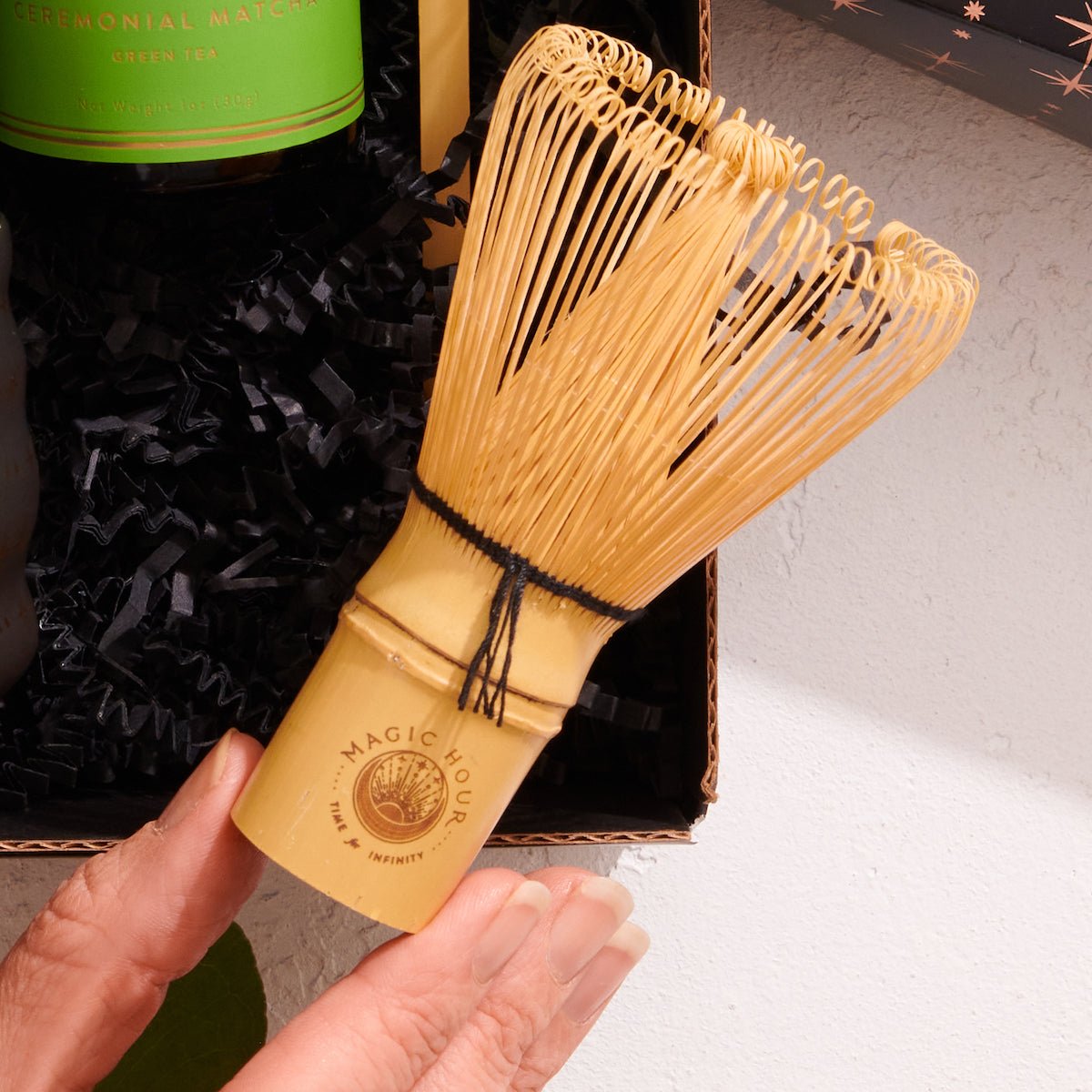 Magic Hour bamboo whisk held by a hand with a branded logo against a neutral background