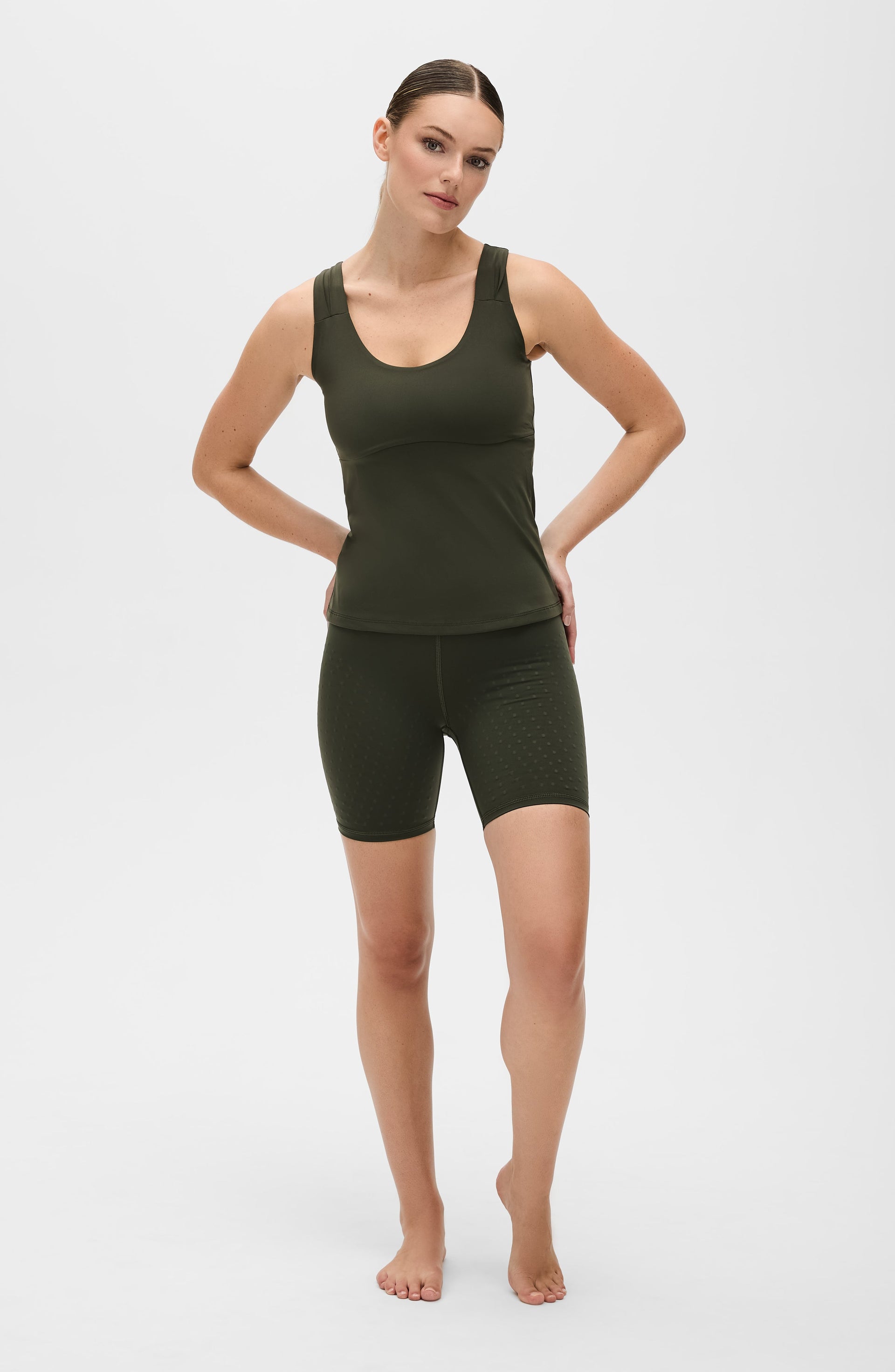 Woman standing with hands on hips while wearing the Elastique Athletics L'Original Lymphatic Bike Short in olive green with a matching sleeveless top.