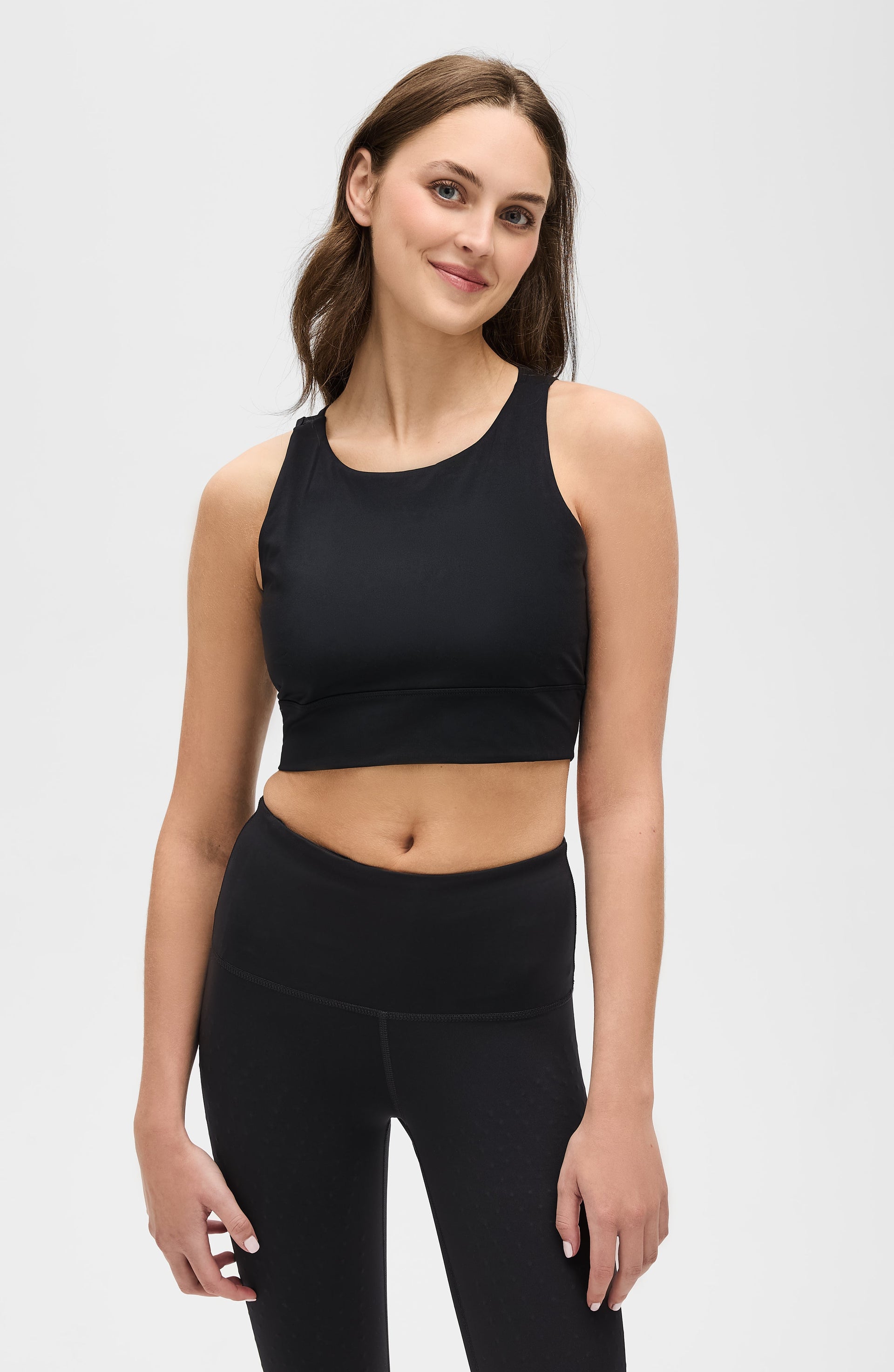Full body studio portrait of a woman wearing the Elastique Athletics L'Original black sports bra and high waisted leggings.