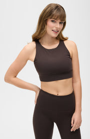 Woman posing in the Elastique Athletics L'Original dark brown sports bra and black leggings in a minimal studio setting.