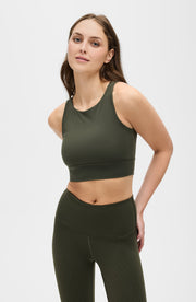 Woman standing with one hand on her hip while wearing the Elastique Athletics L'Original olive green sports bra and matching leggings.