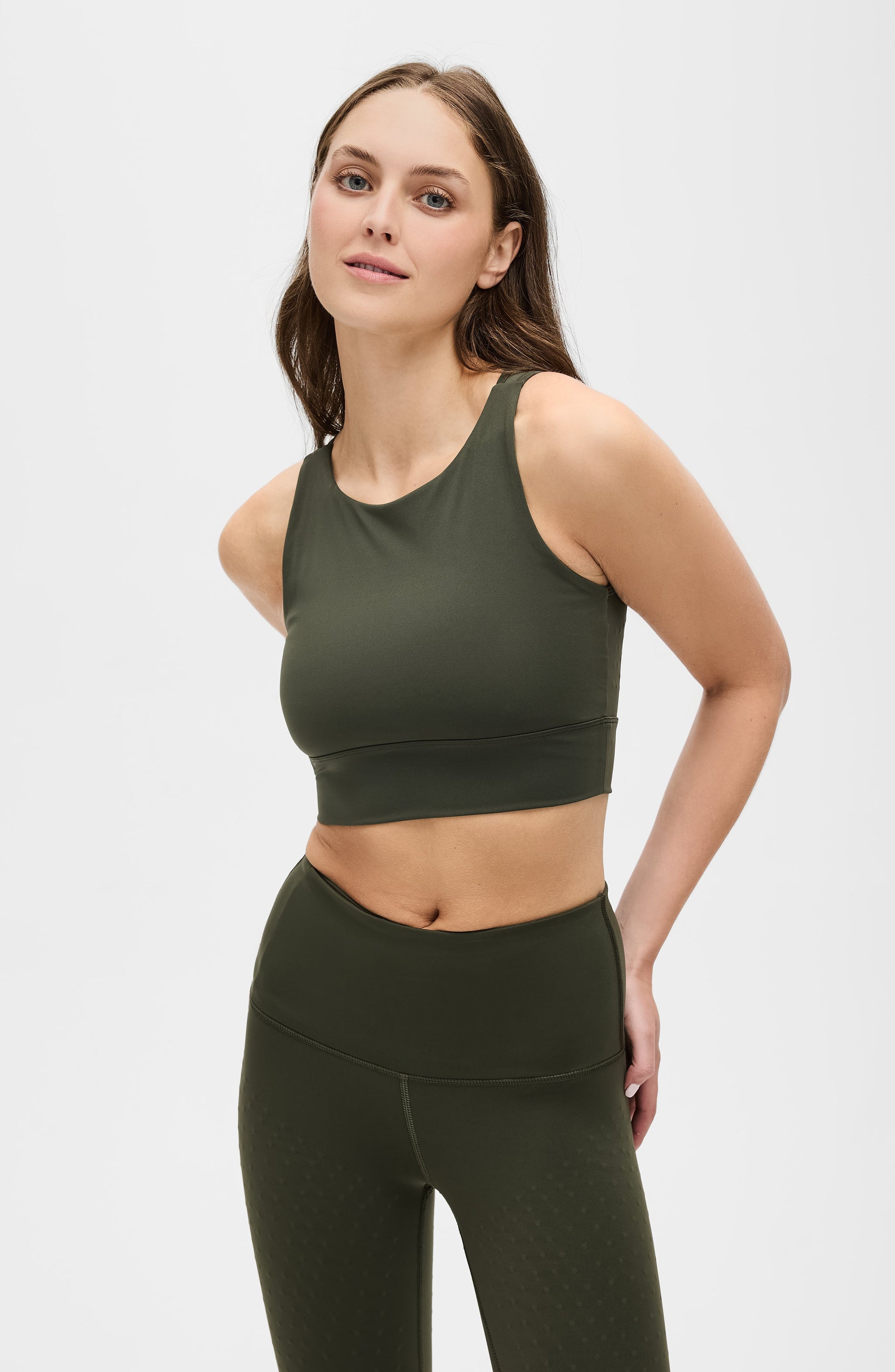Woman standing with one hand on her hip while wearing the Elastique Athletics L'Original olive green sports bra and matching leggings.