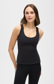 Woman standing with hands behind her back while wearing the Elastique Athletics L'Original Lymphatic Tank in black with matching leggings.