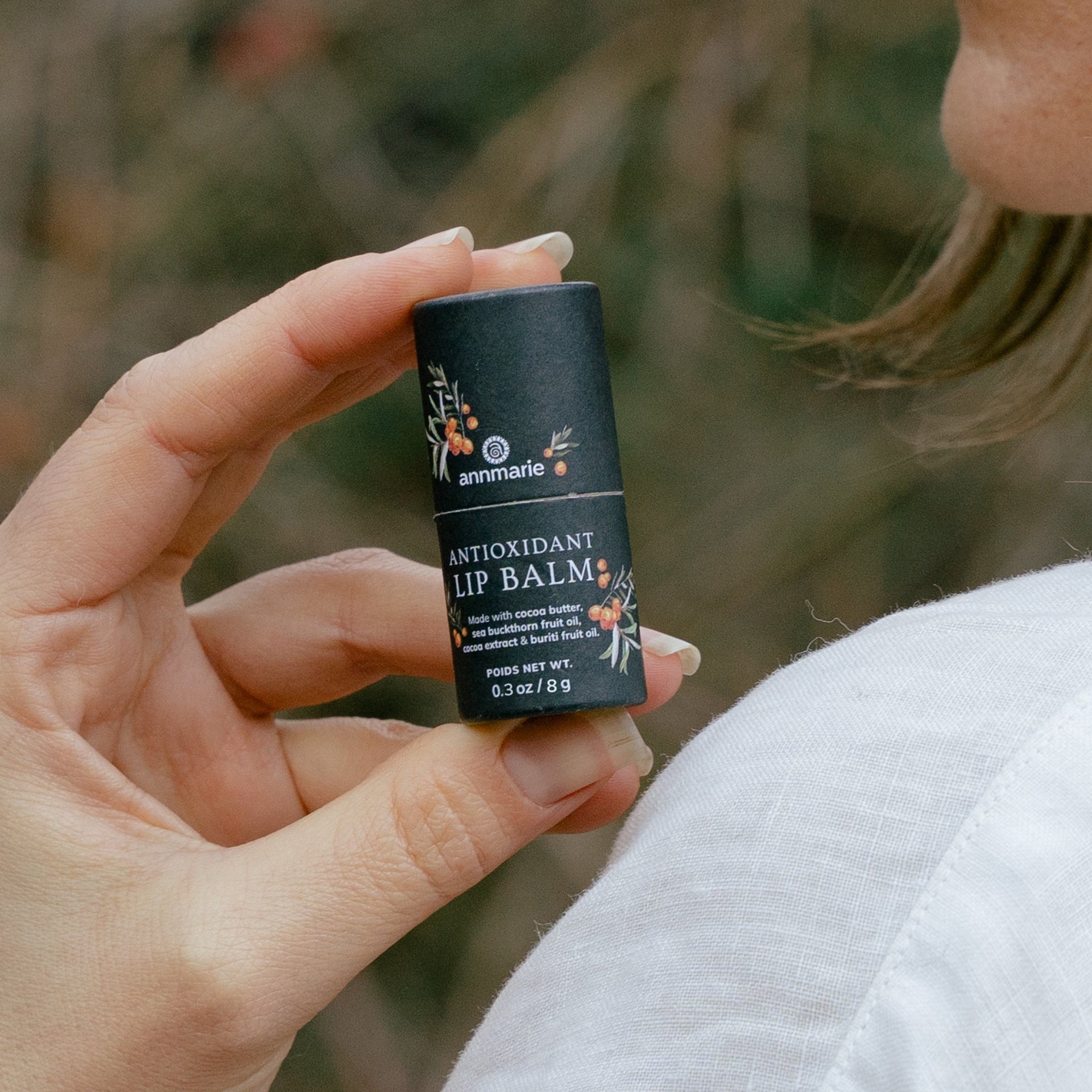 Hand holding Annmarie Antioxidant Lip Balm during an outdoor skincare routine