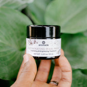 Annmarie Illuminating Pearl Mask brightening facial treatment held in hand against lush green foliage