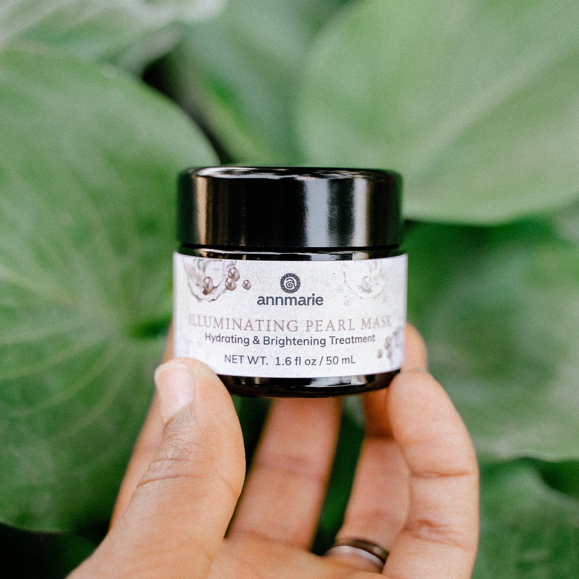 Annmarie Illuminating Pearl Mask brightening facial treatment held in hand against lush green foliage