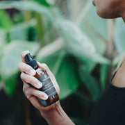 Person applying Annmarie Palo Santo Hair & Body Mist outdoors surrounded by lush greenery