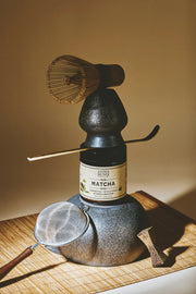 Open jar of Anima Mundi ceremonial grade matcha with bamboo whisk and bright natural styling.