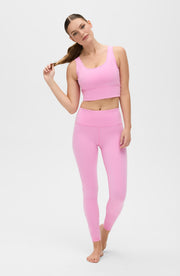 Woman posing with one hand holding her hair while wearing the Elastique Athletics Rise Bra Vie en Rose in soft pink with matching leggings.