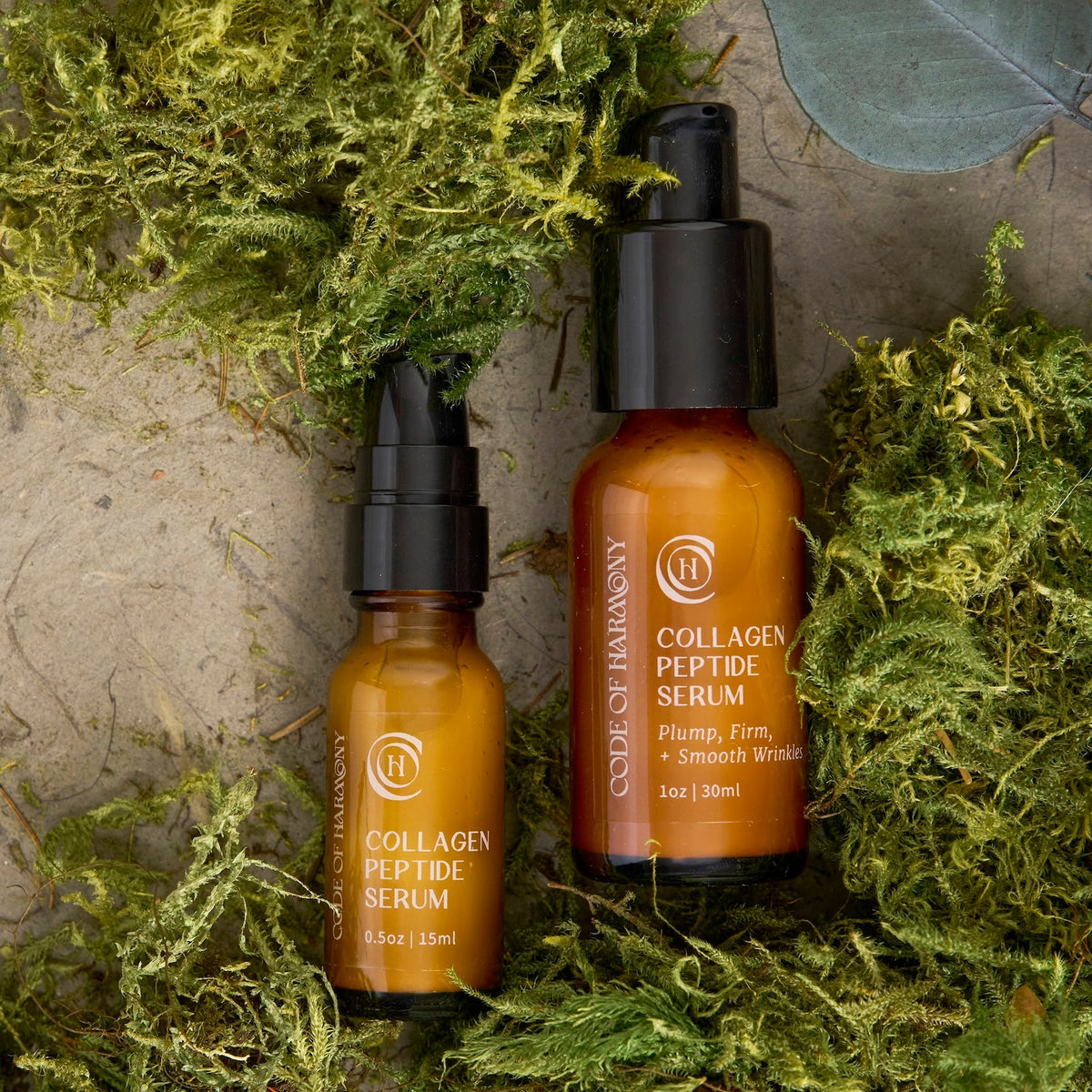 Code of Harmony Collagen Peptide Serum 0.5 oz and 1 oz bottles styled with green moss