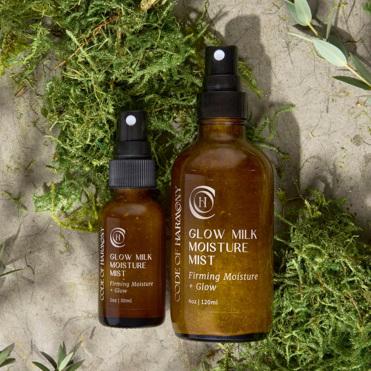 Code of Harmony Glow Milk Moisture Mist 1 oz and 4 oz bottles styled with green moss