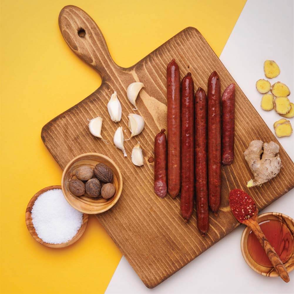 Grass-fed beef sticks on cutting board with natural ingredients like garlic, ginger, and spices