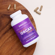 Paleovalley Grass Fed Organ Complex supplement bottle on a wooden tray with capsules, featuring a freeze-dried blend of grass fed beef liver, heart, and kidney.