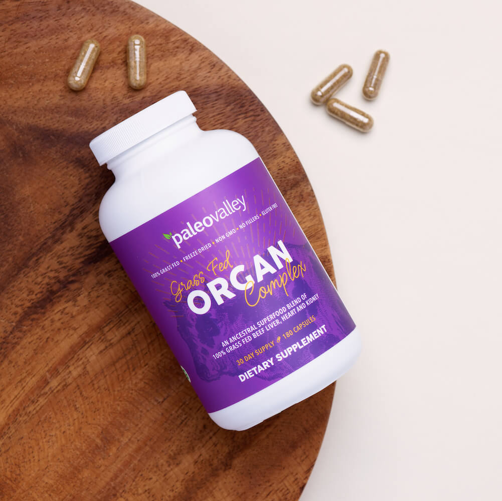Paleovalley Grass Fed Organ Complex supplement bottle on a wooden tray with capsules, featuring a freeze-dried blend of grass fed beef liver, heart, and kidney.