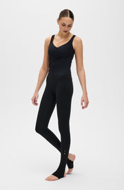 Full body studio portrait of a woman walking barefoot while wearing the Elastique Athletics L'Original Lymphatic Stirrup Leggings in black with a matching tank top.