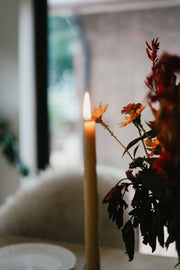 Lit Busy Bees Hand Dipped 12 Inch Taper Candles displayed beside floral arrangements in a warm indoor setting.