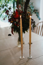 Tall lit Busy Bees taper candles from The Queen Bee Bundle displayed beside floral arrangements in an elegant interior setting.